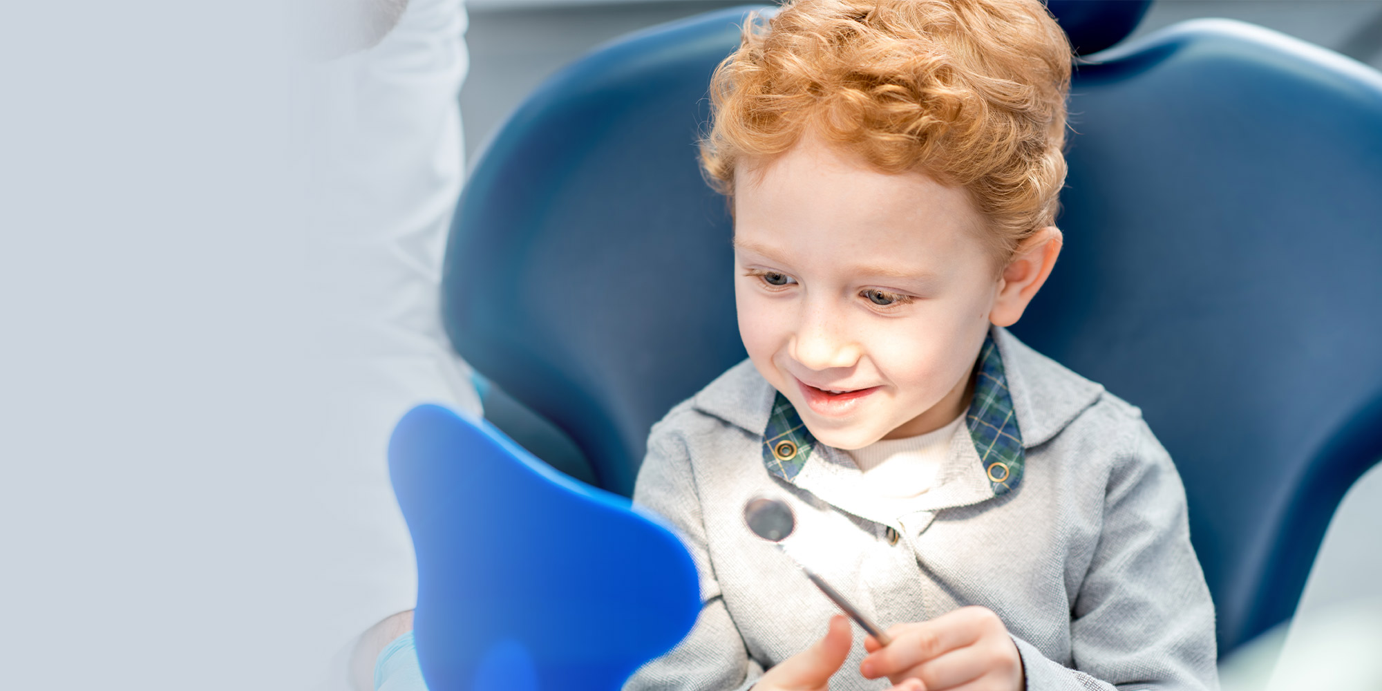 Kid with red hair sitting in dental chair learning about dental tools