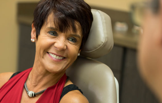 woman sitting in a dentist office smiling after getting full mouth dental implants.