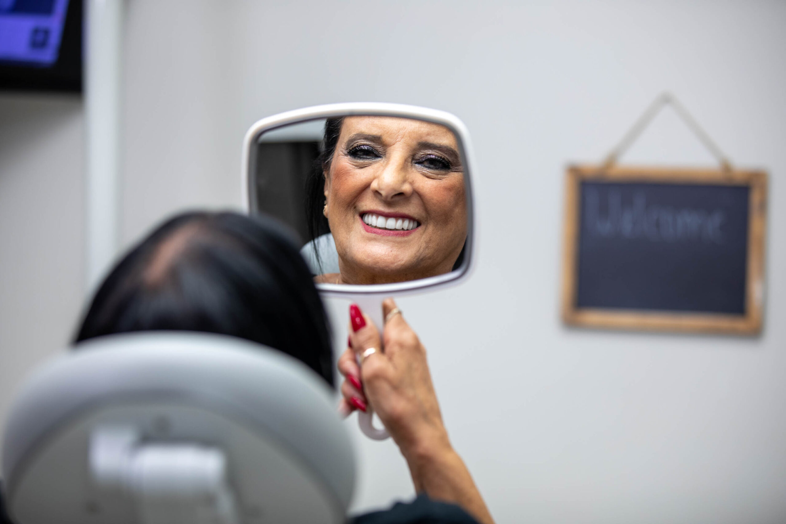 a patient admiring her smile in a hand held mirror after Dr. Azar has treated her with Invisalign.